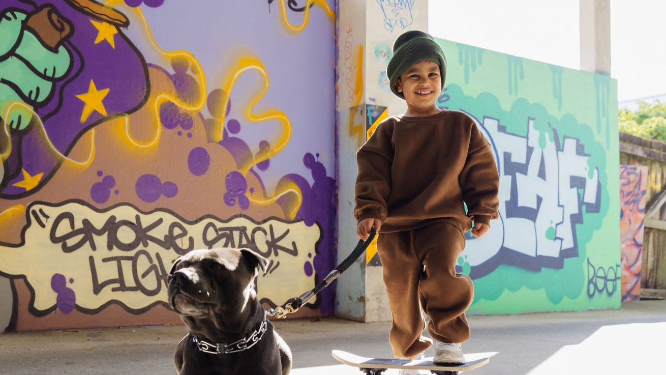 Child in Downtown Set in espresso standing next to a dog on a skateboard in front of graffiti-covered walls | Crumb Clothing NZ | Crumb.co.nz