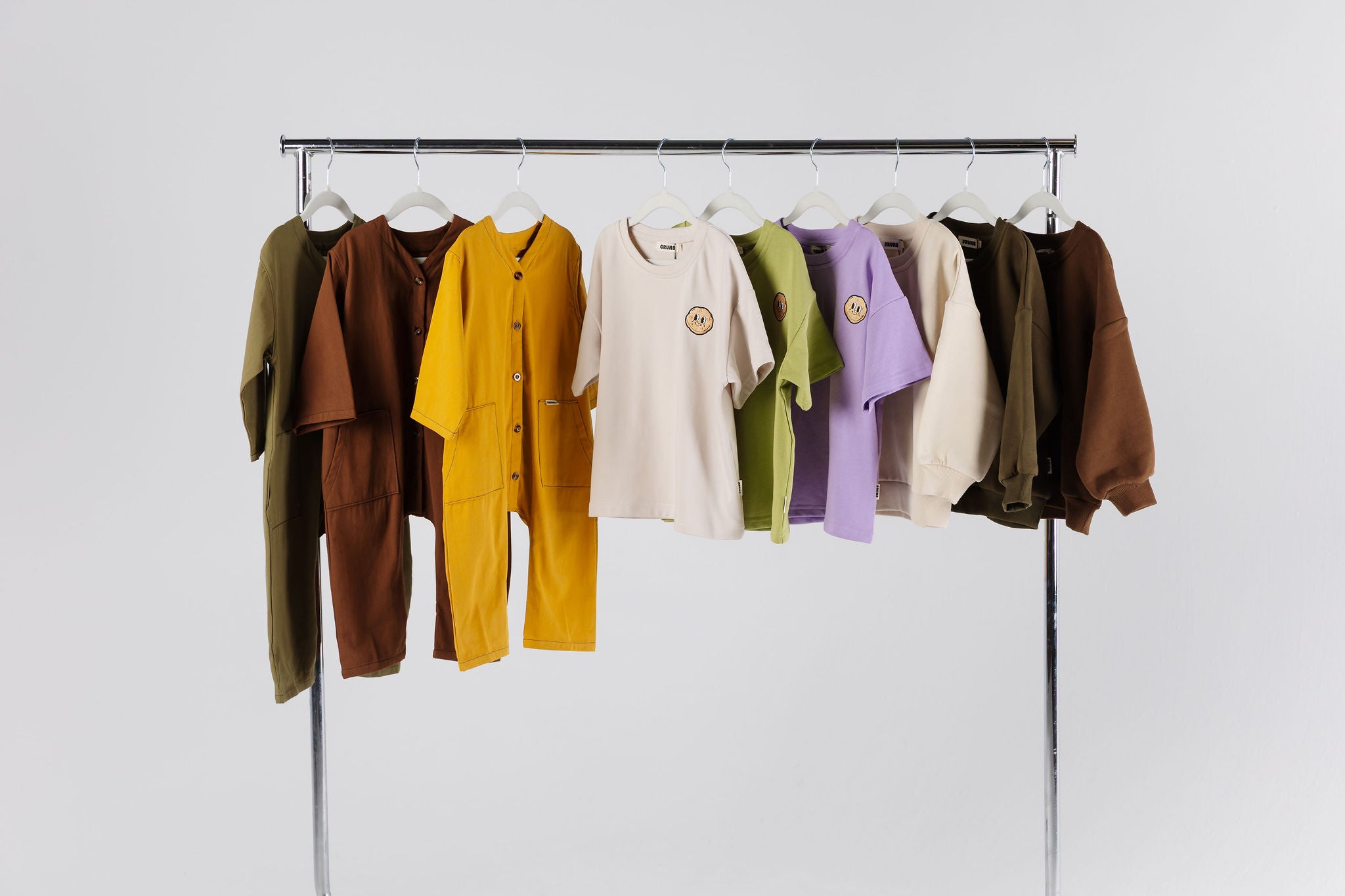 Crumb.co.nz Clothing rack with various colored outfits on a plain a white background.