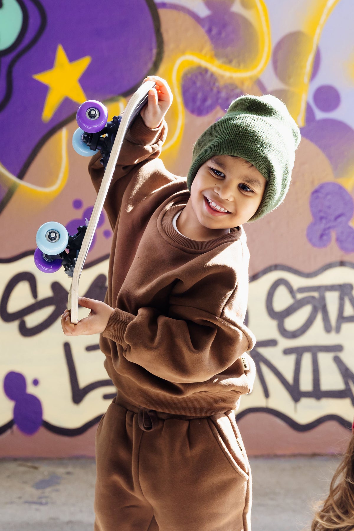 Child in Crumb Clothing Downtown Set in Espresso Chocolate against a colorful graffiti wall.